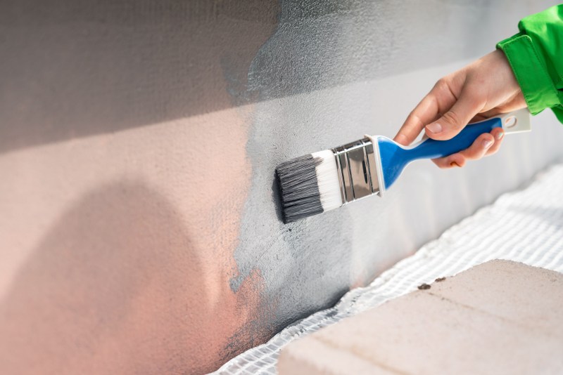 Loseup Of Hand With Paint Brush Painting Building Exterior Wall 1